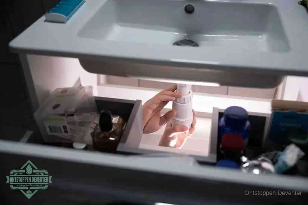 Een pompfles met zeep boven een wastafel, de heet water en afwasmiddel-methode om een vetprop in de afvoer los te maken in Deventer