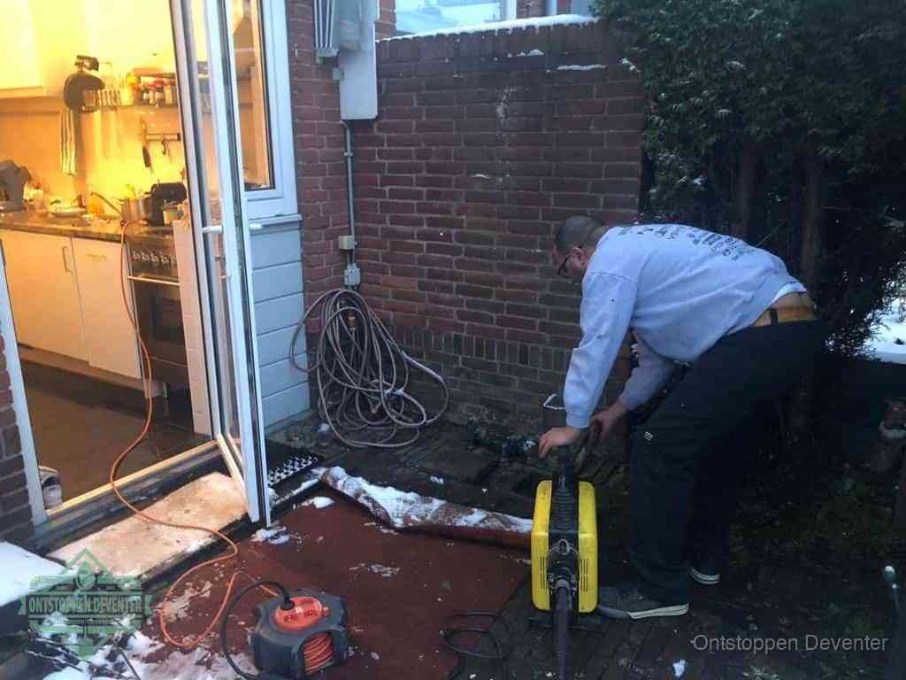 Een monteur werkt buiten bij een open riool-/grondput met een elektrische ontstoppingsmachine om een verborgen afvoerprobleem op te sporen in Deventer