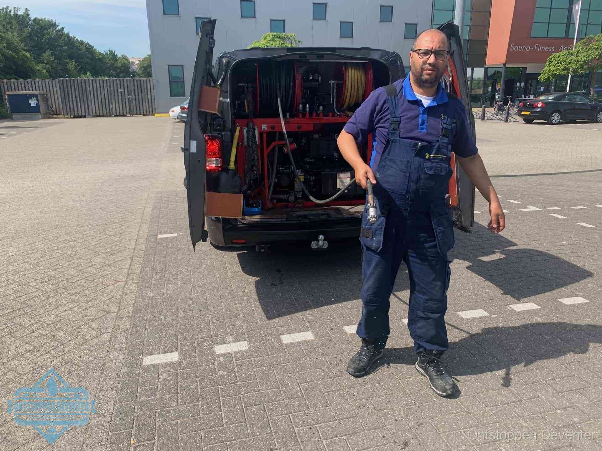 Een monteur bij zijn bestelbus met een hogedruk- en rioolreinigingsunit, klaar om de oorzaak van terugkerende wc-verstoppingen aan te pakken in Deventer