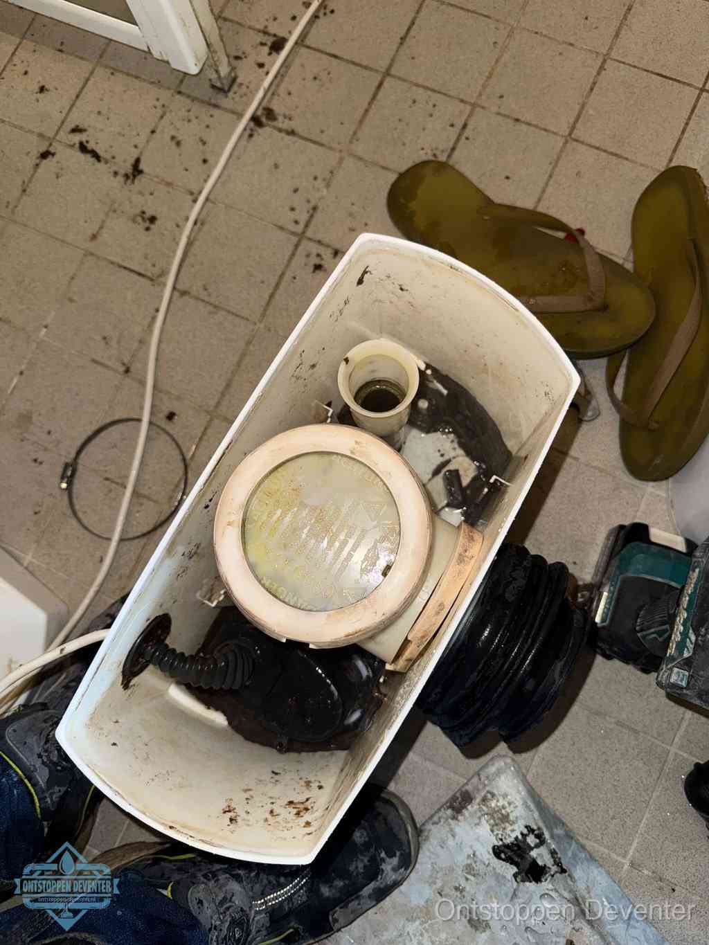 Een gedemonteerde toiletpot op de vloer met ontstoppingsveer en gereedschap ernaast, het verwijderen van een vastzittend voorwerp uit de wc in Deventer