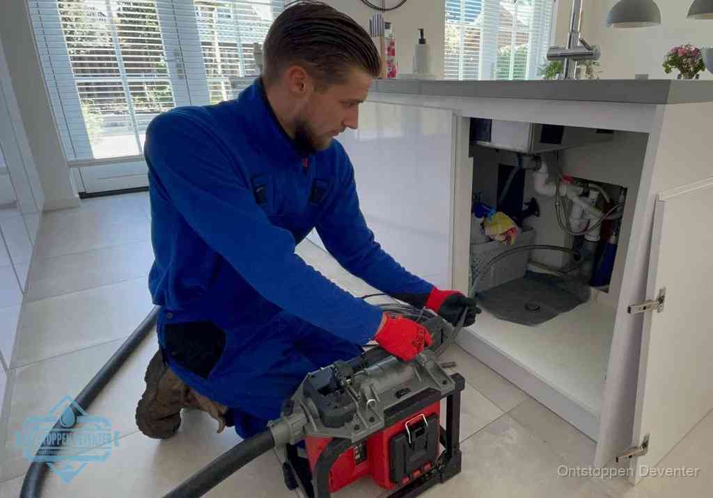 Een monteur voert een professionele elektrische ontstoppingsmachine in de afvoer onder de spoelbak tijdens het gootsteen ontstoppen in Deventer