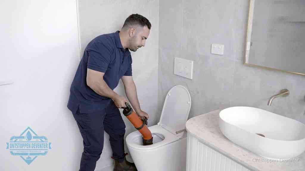 Een man gebruikt een handmatige luchtdruk-ontstopper in een modern betegeld toilet om zelf de wc te ontstoppen in Deventer